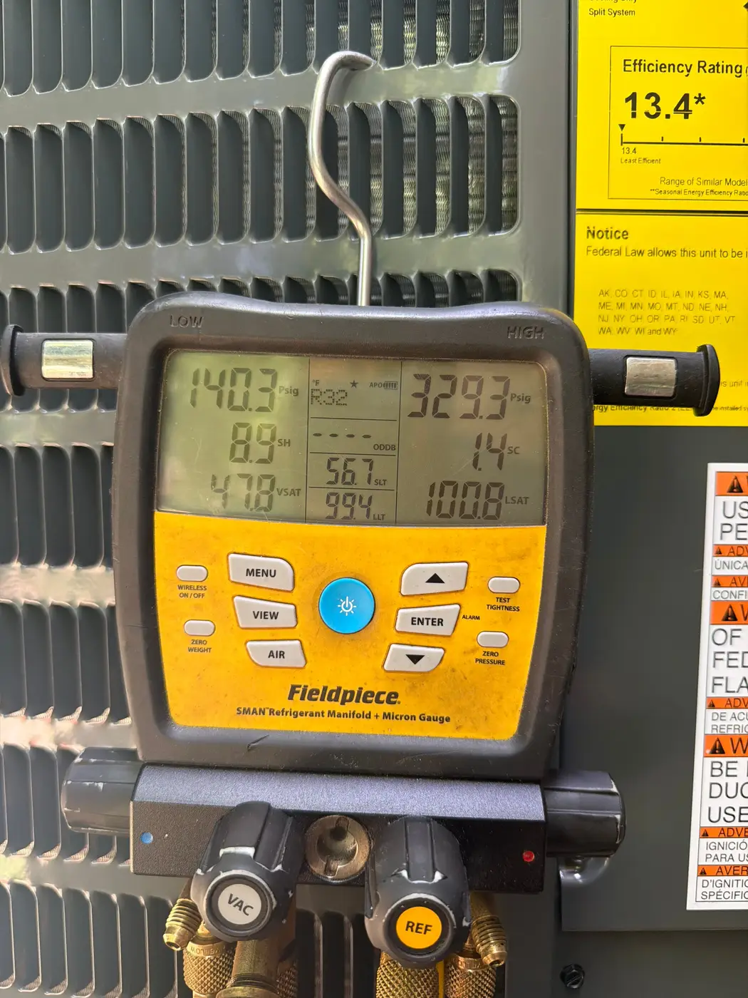 Digital refrigerant gauge hung on an outdoor AC unit, hoses connected