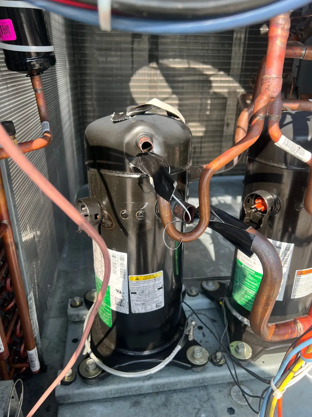 Two compressors inside an outdoor condensing unit with copper refrigerant piping