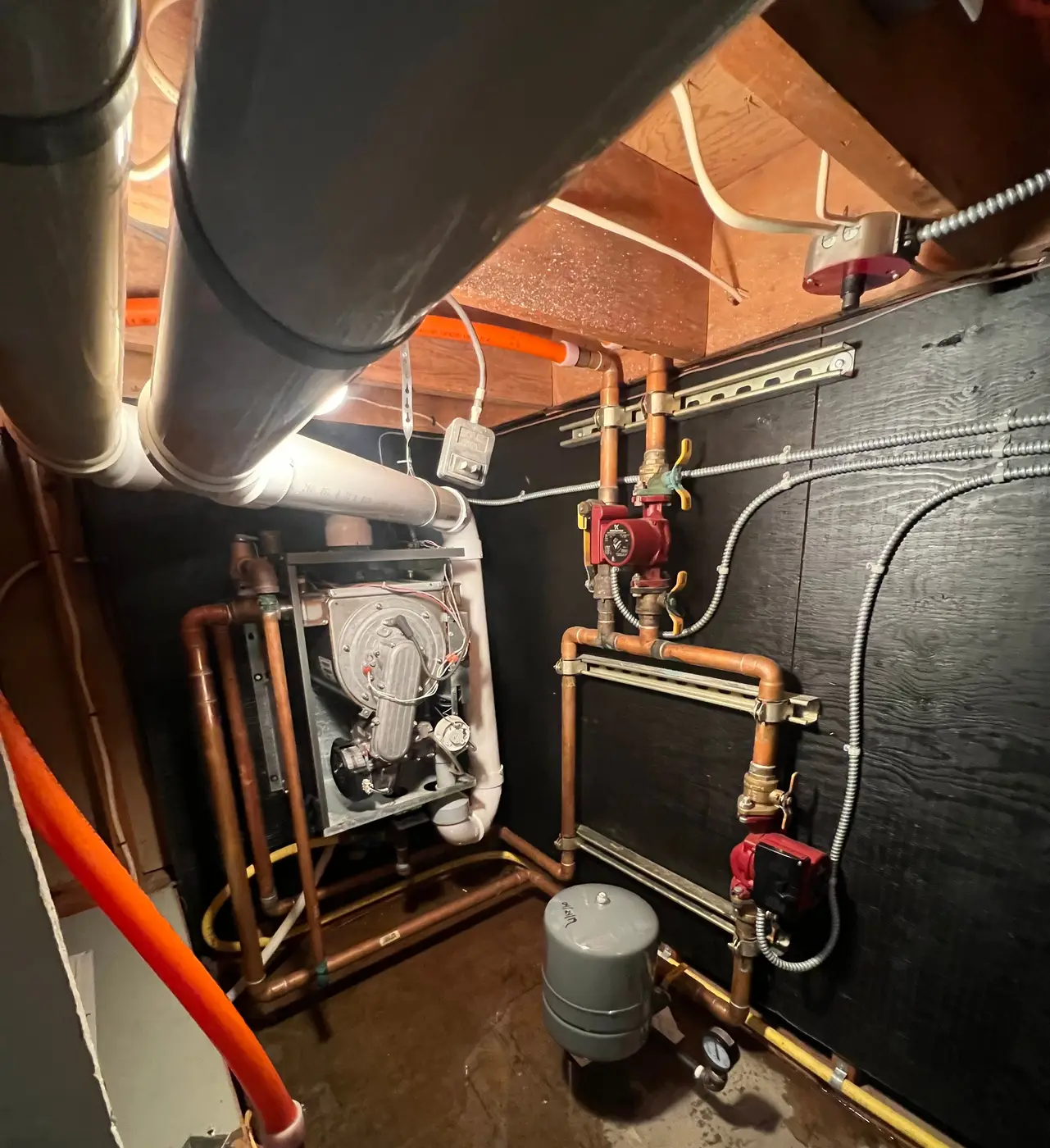 Wall-hung boiler with copper piping, two circulator pumps and an expansion tank on a black backboard
