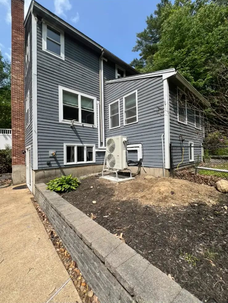 Heat pump outdoor unit on a stand beside a gray-sided house