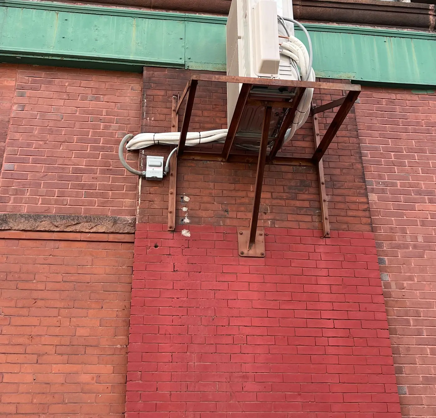 Heat pump outdoor unit on a steel wall bracket high on a brick building