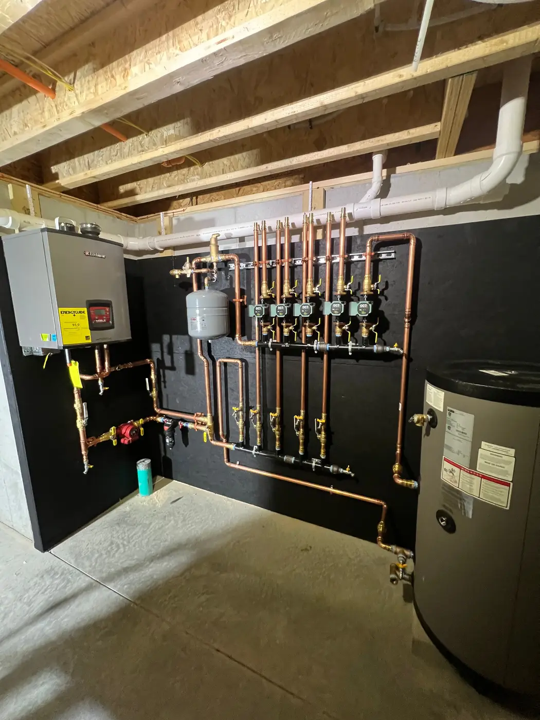Indirect water heater tank piped to a wall-hung boiler and zone circulators in a basement
