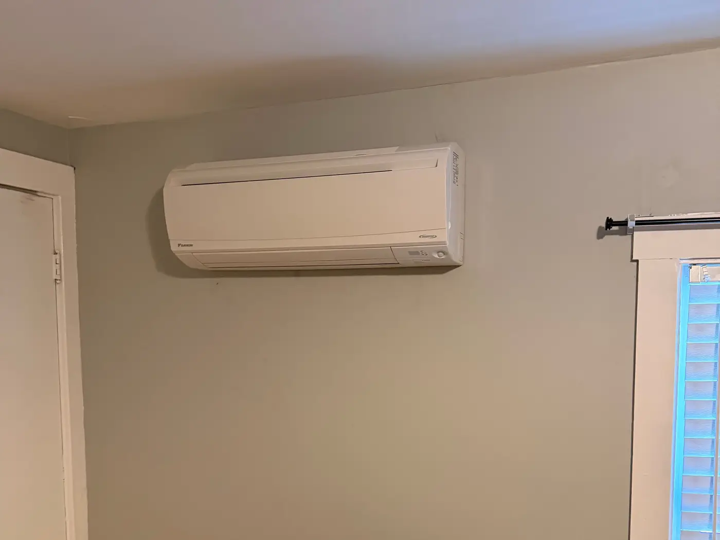 Ductless mini-split head mounted high on a bedroom wall beside a window