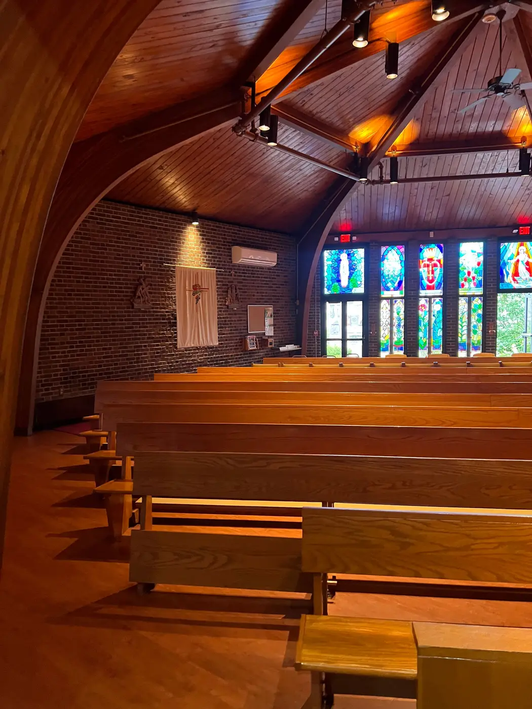 Ductless mini-split head on the brick wall of a church with wooden pews and stained glass windows