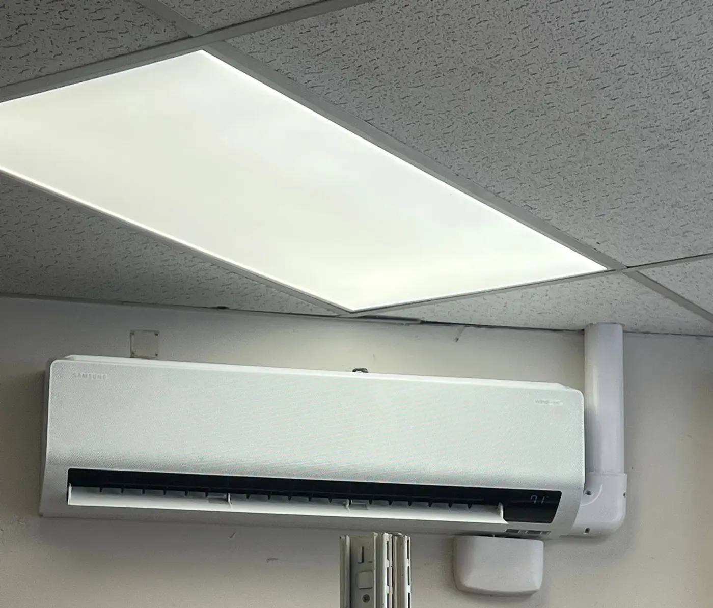 Ductless mini-split head mounted on a wall below a drop ceiling in a store