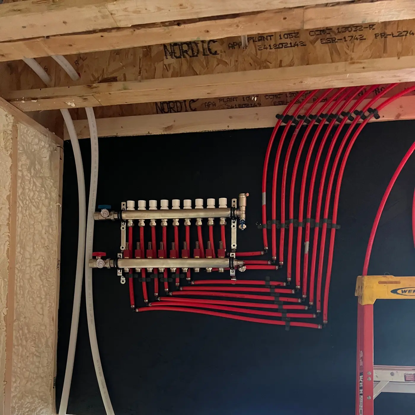Radiant floor heating manifold on a black backboard with red PEX tubing running to the floor