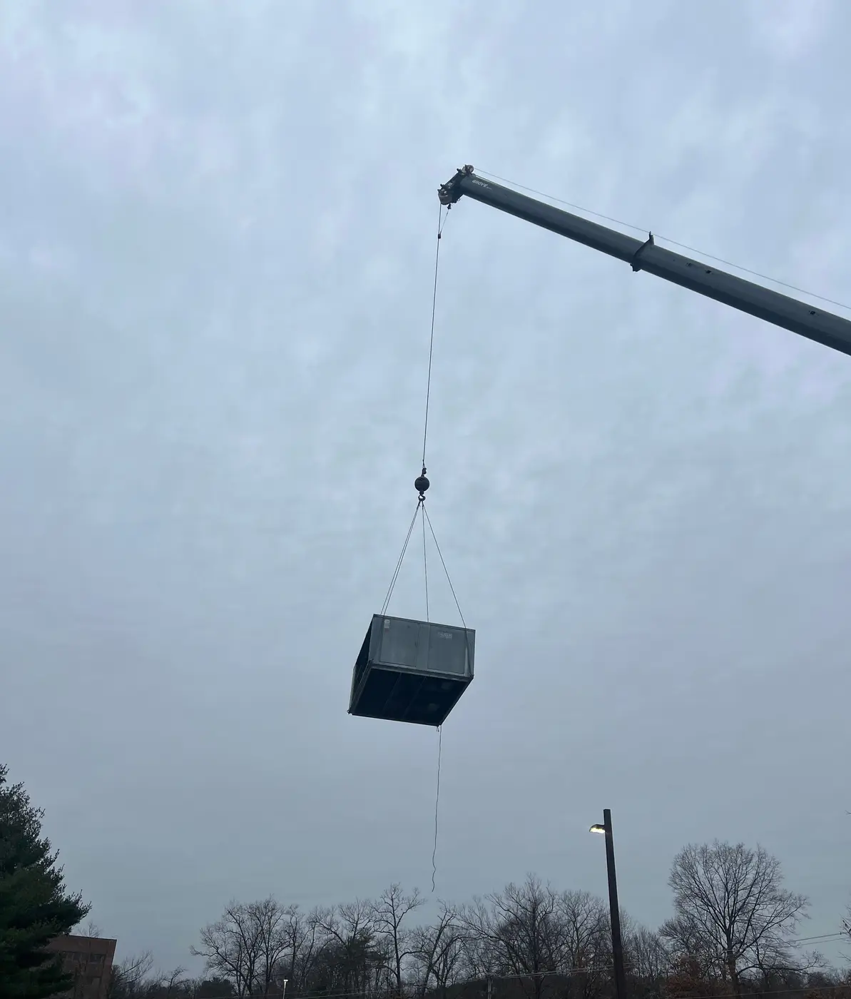 Crane lifting a commercial rooftop unit against a gray sky